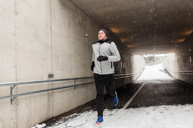 fitness, esporte, pessoas, temporada e conceito de estilo de vida saudável - jovem feliz correndo ao longo do túnel de metrô de pedestres no inverno
