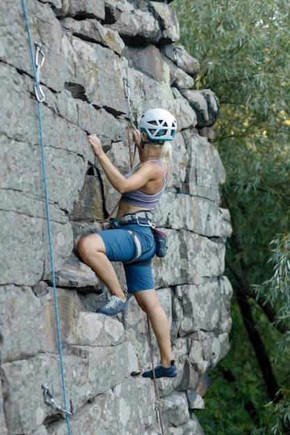 Fitness, esporte radical e conceito de estilo de vida saudável - Climber supera uma rota de escalada desafiadora. Uma garota sobe em uma rocha. Mulher envolvida em esportes radicais. Hobby extremo.