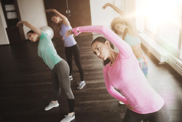 fitness, esporte, treinamento, ginásio e conceito de estilo de vida - grupo de mulheres felizes malhando e alongando na academia