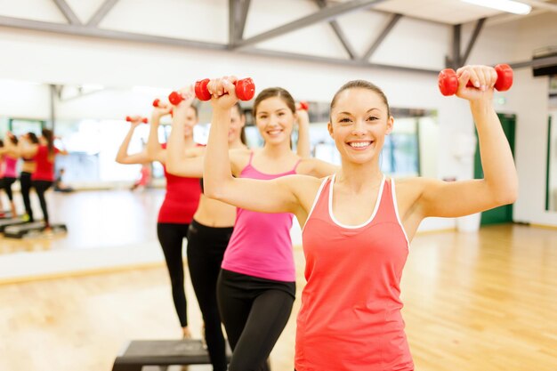 fitness, esporte, treinamento, ginásio e conceito de estilo de vida - grupo de mulheres sorridentes com halteres e passo aeróbico