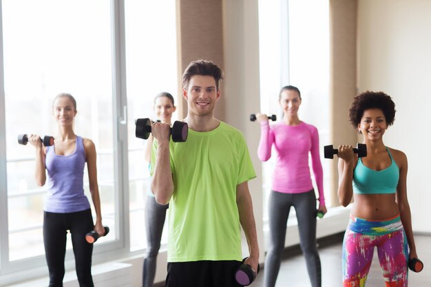 fitness, esporte, treinamento, ginásio e conceito de estilo de vida - grupo de pessoas sorridentes malhando com halteres flexionando os músculos no ginásio