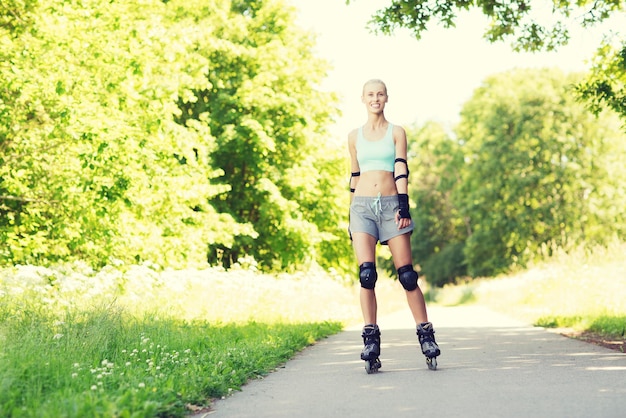 fitness, esporte, verão, patins e conceito de estilo de vida saudável - jovem feliz em patins e equipamento de proteção andando ao ar livre