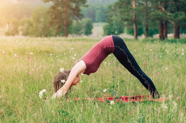 Fitness, esportes, ioga na natureza Conceito de felicidade de saúde. mulher morena com top cor de vinho e legging preta fazendo ioga na natureza
