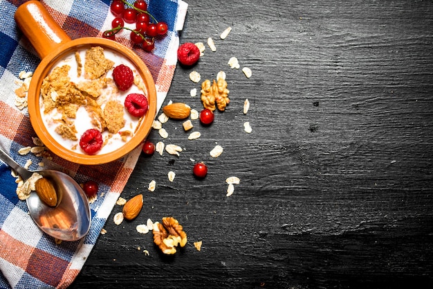 Fitness Essen. Müsli mit Beeren, Nüssen und Milch in der Schüssel auf schwarzem Holztisch.