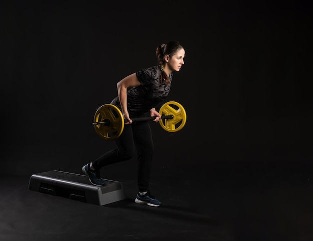 Fitness-Frau auf der Stufenplattform mit einer Langhantel gelbe Pfannkuchen zieht ihr Bein Engagiert im Sport