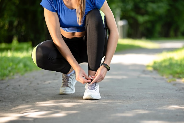 Fitness-Frau, die an einem sonnigen Morgen Schnürsenkel in Laufschuhen beim Outdoor-Training im Park bindet