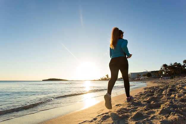 Fitness-Frau, die bei Sonnenuntergang am Meer läuft.