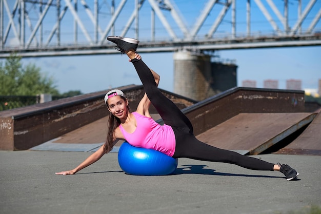 Fitness-Frau, die Dehnübungen mit Fit-Ball auf städtischem Hintergrund macht