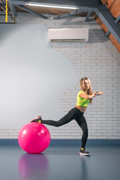 Fitness-Frau führt Übung mit Fitness-Ball durch Sportmädchen in Leggings und Top posiert mit Sportgeräten