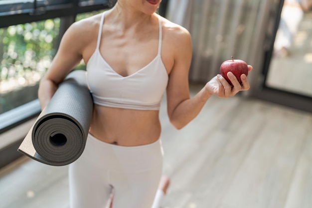 Fitness-Frau hält Yogamatte mit frischem Apple Heathy, sauberem veganem Essen, bevor sie im Yoga-Studio trainiert