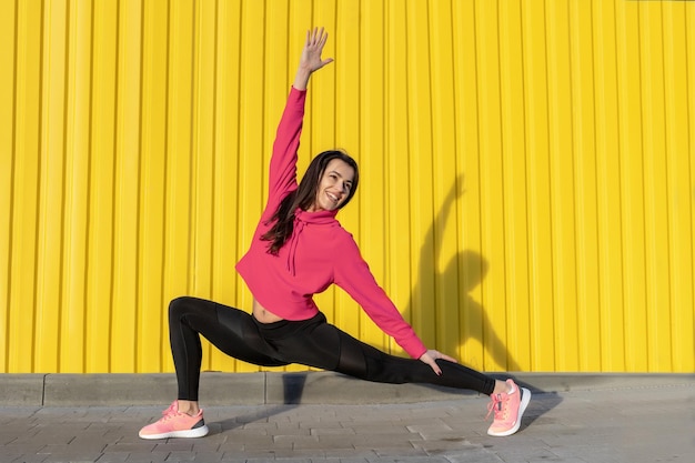 Fitness-Frau ist Fitness, die sich im Freien in der städtischen Umgebung der gelben Wand ausdehnt und trainiert