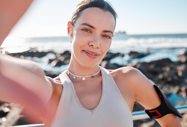 Fitness-Frau und Porträtlächeln für Selfie-Vlog oder Profilbild am Strand für Laufübungen Fröhliche Läuferin lächelt für Social-Media-Speicher oder Post an der Meeresküste für gesundes Wohlbefinden