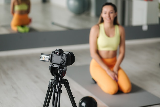 Fitness-Frauentrainer, der Videoo vor der Kamera aufzeichnet, während im Fitnessstudio im Innenbereich trainiert. Konzept Lifestyle Influencer Sport und Erholung.