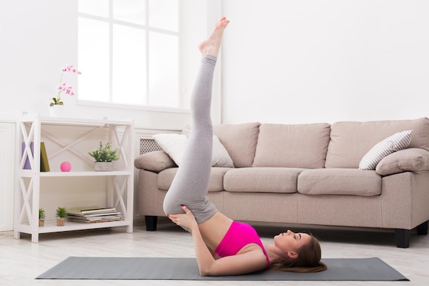 Fitness, Frauentraining Yoga in Schulterstand-Pose zu Hause. Junges schlankes Mädchen macht Übung.