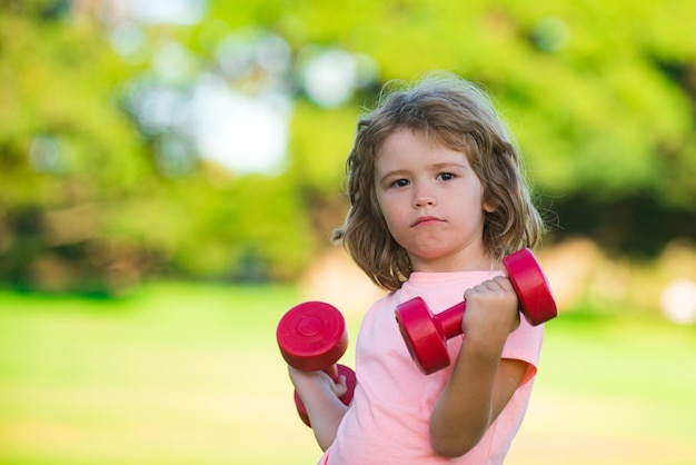 Fitness Hanteln Kindertraining im Freien. Junge sportliches Kind mit Hanteln. Sportportrait Kinder.