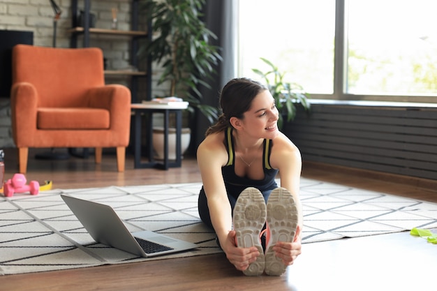 Foto fitness hermosa mujer delgada haciendo ejercicios de estiramiento de fitness en casa en la sala de estar. quédese en las actividades de la casa. deporte, estilo de vida saludable.