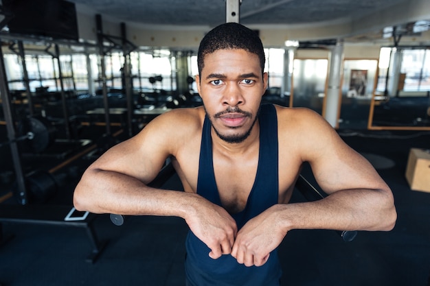 Fitness hombre afroamericano descansando en el gimnasio después del entrenamiento y mirando a cámara