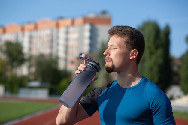 Fitness hombre bebiendo agua durante el entrenamiento en el estadio. Concepto de estilo de vida saludable. Espacio para texto