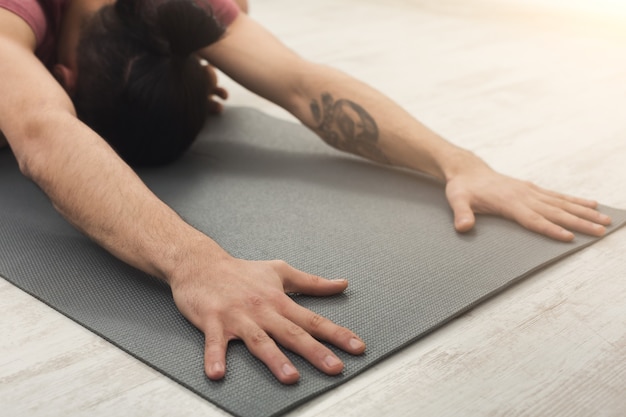 Fitness, hombre entrenando yoga en pose de niño, copie el espacio. Chico joven deportivo hace ejercicio aeróbico en la colchoneta en el gimnasio