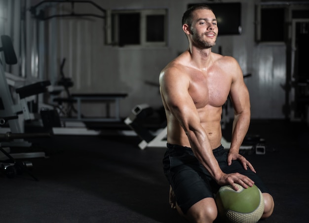 Fitness hombre posa con una pelota en el gimnasio