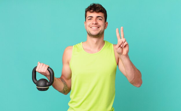 Fitness hombre sonriendo y mirando amigable, mostrando el número dos o el segundo con la mano hacia adelante, contando hacia atrás