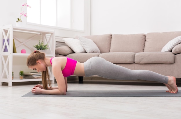 Fitness, ioga de treinamento de mulher na prancha em casa. Jovem magro faz exercício.