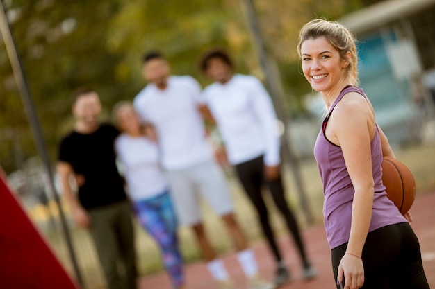 Fitness jovem mulher com bola de basquete, jogando jogo ao ar livre com amigos