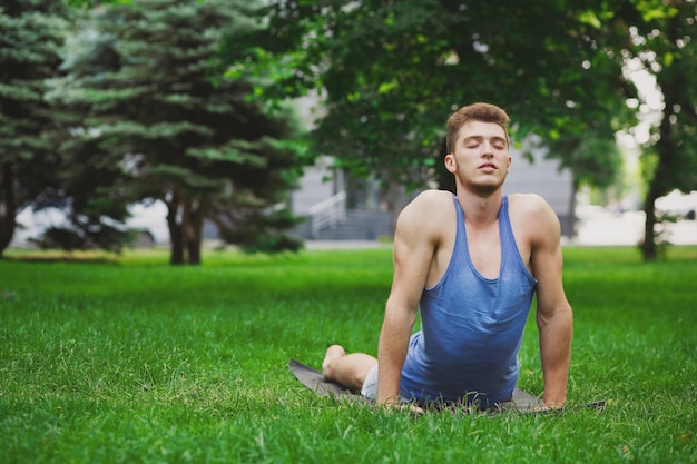 Fitness, joven entrenamiento de yoga en pose de cobra en el parque. Chico deportivo con los ojos cerrados hace ejercicio al aire libre, espacio de copia