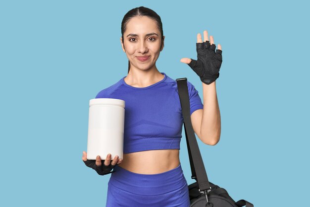 Foto fitness joven mujer blanca con proteínas y bolsa en el fondo del estudio sonriendo alegre