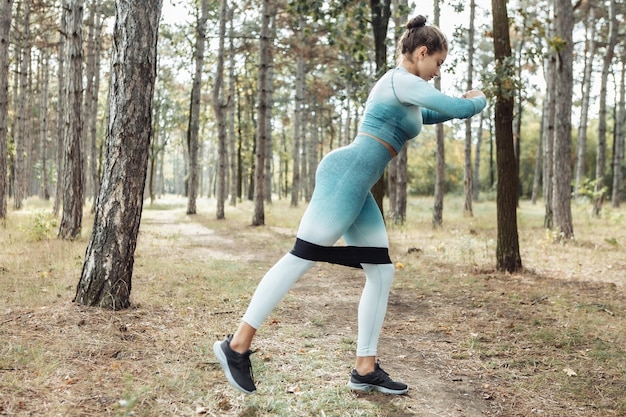 Fitness joven mujer con cabello rizado haciendo ejercicio con bandas de goma de fitness en el bosque