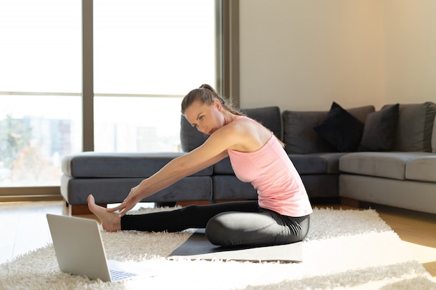 Fitness en línea Mujer joven haciendo ejercicios en estera de yoga frente a la computadora portátil