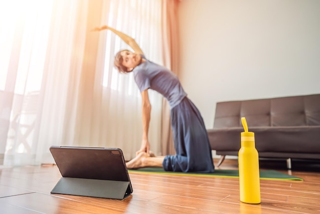 Fitness man haciendo ejercicio en el suelo en casa y viendo videos de fitness en una tableta La gente hace deportes en línea debido al coronovirus