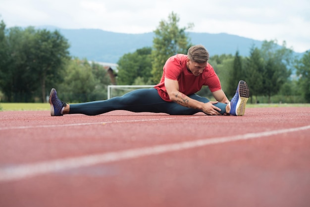 Fitness-Mann, der sich vor dem Training ausdehnt und auf der Strecke läuft