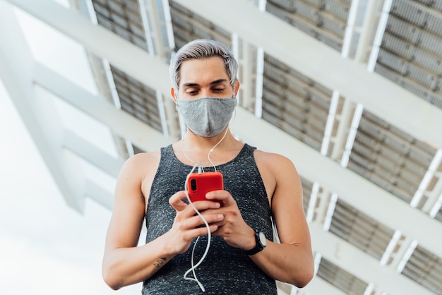Fitness-Mann in der Maske unter Verwendung eines Smartphones mit Kopfhörern