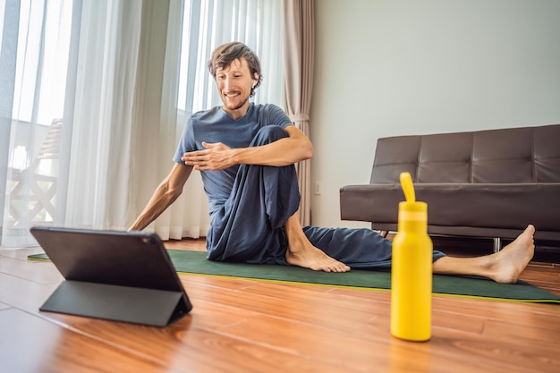 Fitness-Mann trainiert zu Hause auf dem Boden und schaut sich Fitnessvideos auf einem Tablet an Wegen des Coronovirus treiben Menschen online Sport