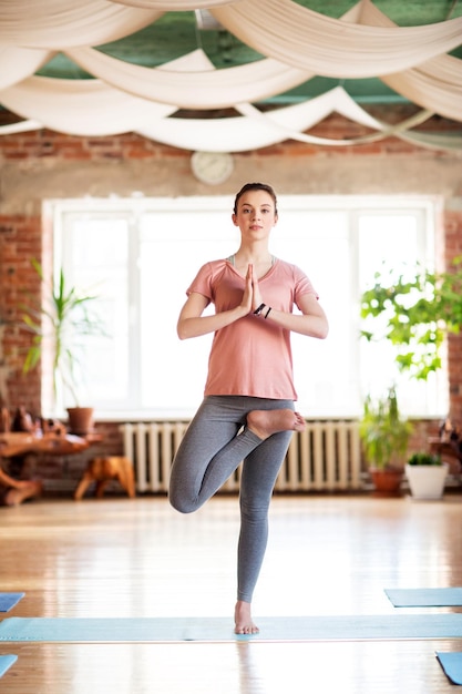 Fitness, Menschen und gesundes Lebensstilkonzept – junge Frau macht Yoga in Baumpose im Studio