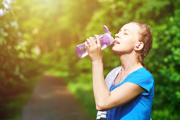 Fitness mujer agua potable después de correr entrenamiento en el parque de verano