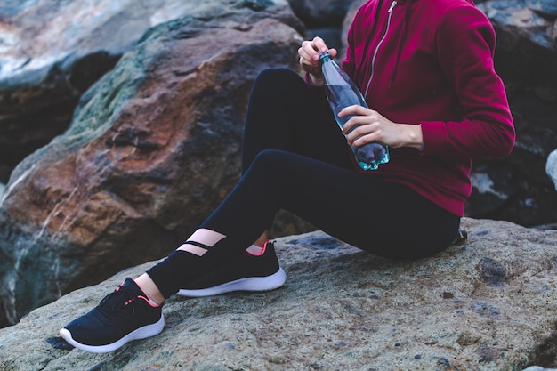 Fitness mujer atractiva en zapatillas sentado en una piedra