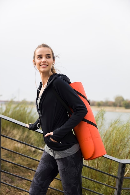 Fitness mujer caminando con colchoneta en la espalda al aire libre