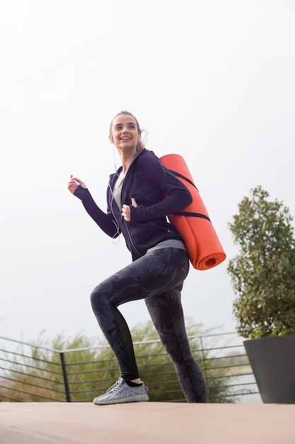 Fitness mujer caminando con colchoneta en la espalda