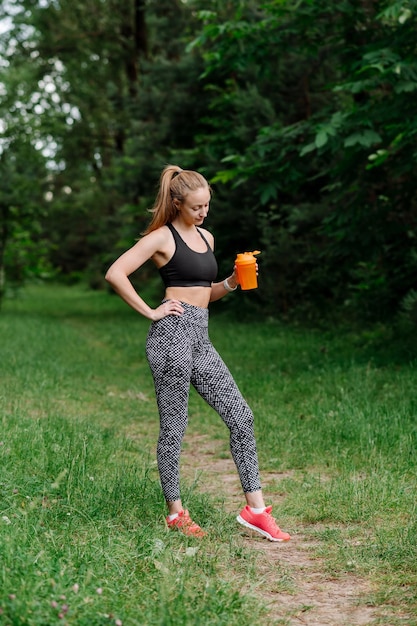 Fitness mujer deportiva en ropa deportiva con botella de agua después de los entrenamientos en el parque