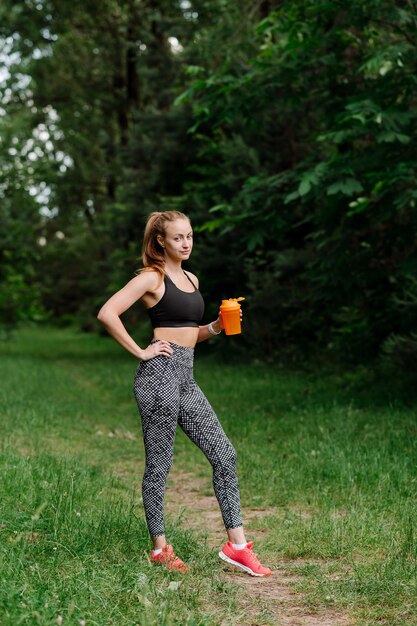 Fitness mujer deportiva en ropa deportiva con botella de agua después de los entrenamientos en el parque