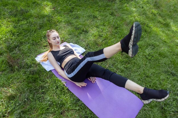 Fitness mujer entrena los músculos abdominales haciendo ejercicio acostado sobre una alfombra en la hierba