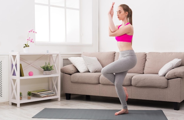 Fitness, mujer entrenando yoga en pose de águila en casa. Joven delgada hace ejercicio.