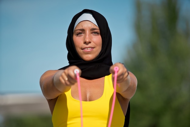 Fitness mujer musulmana con hijab en ropa deportiva amarilla aislada con saltar la cuerda. Vista horizontal de la mujer árabe entrenando al aire libre