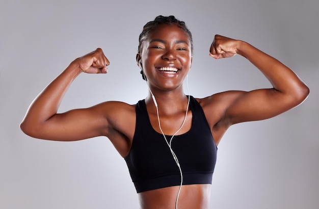 Fitness mujer negra y música con flexión del bíceps en retrato para la felicidad del ejercicio y los objetivos de entrenamiento Sonrisas deportivas y persona femenina con auriculares para escuchar podcast o audio para el entrenamiento