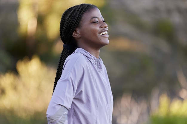 Fitness de mujer negra y pensamiento feliz en la naturaleza en un descanso con una sonrisa alegre Felicidad bienestar y salud de una joven satisfecha con ejercicio cardiovascular y ejercicio descansando