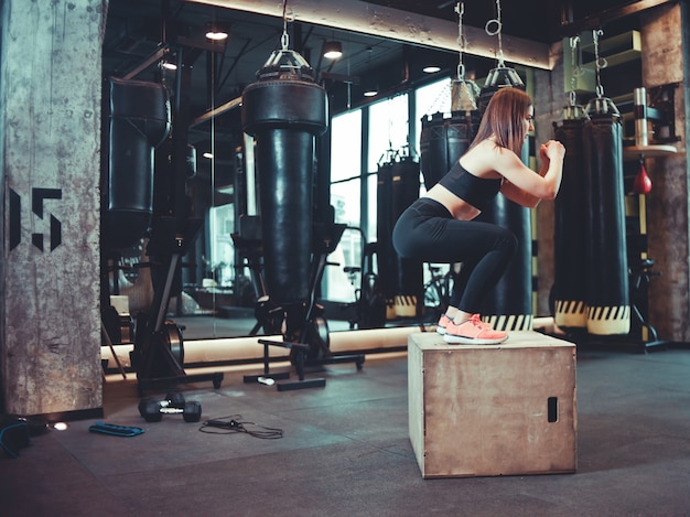 Fitness mujer saltando sobre entrenamiento de caja de madera en el gimnasio