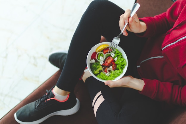 Foto fitness mujer en zapatillas y ropa deportiva está descansando y comiendo una ensalada fresca y saludable después de un entrenamiento. concepto de estilo de vida saludable.