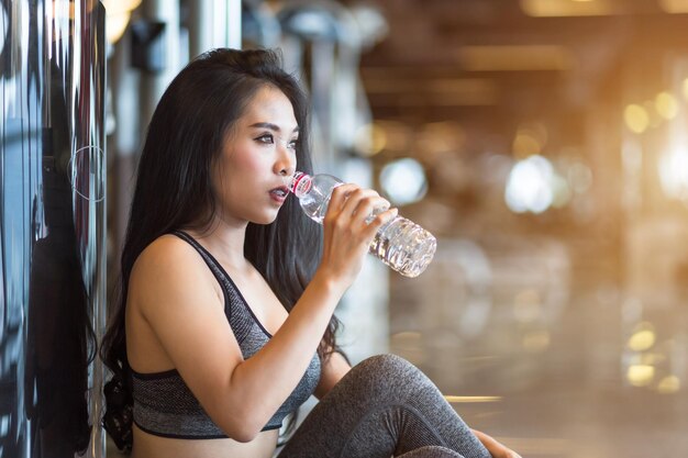 Fitness Mujeres asiáticas sentadas en el interior del gimnasio deportivo y en el club de salud con una botella de agua